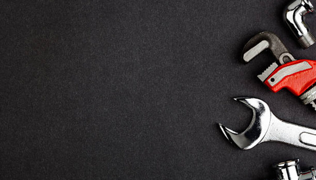 Pipe wrenches, angle and t-connector on textured dark grey and black background.